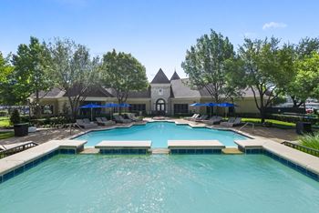 A swimming pool with lounge chairs and umbrellas in front of a building